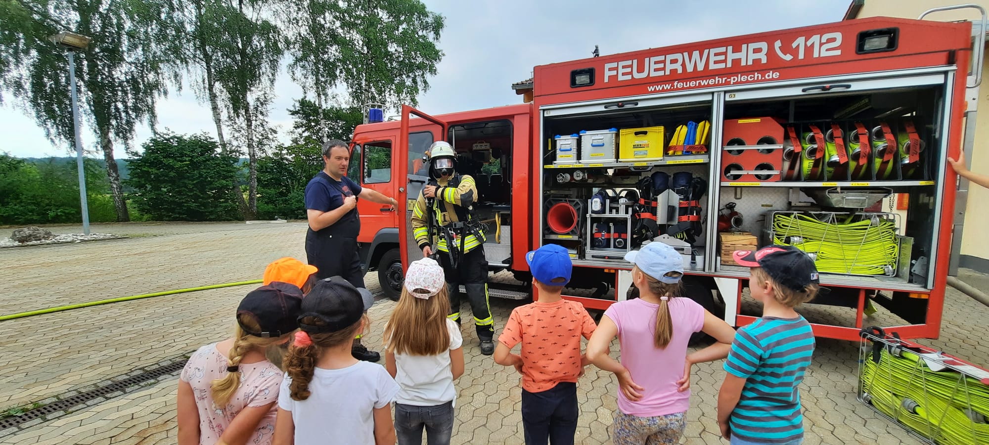 Kinder vor dem Feuerwehrauto während der Kommandant einen Kameraden mit schweren Atemschutz vorstellt.